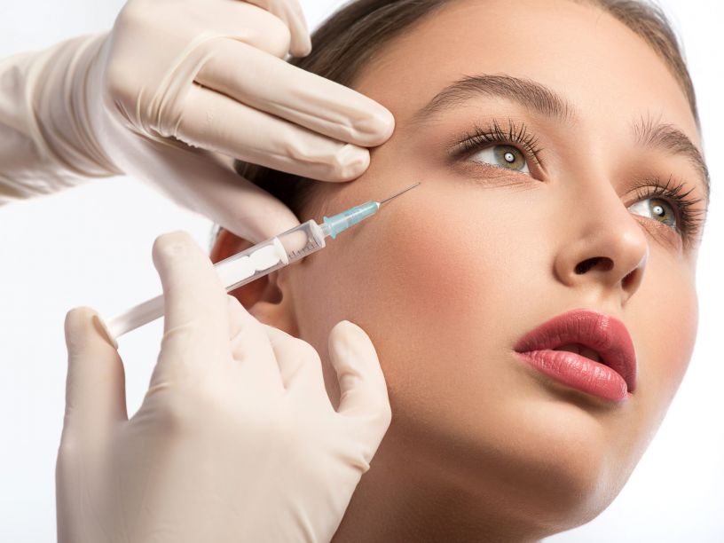 Serine young woman is getting facial botox injection. Beautician hands in gloves holding syringe near her face